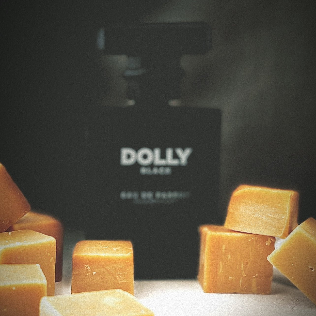 Black DOLLY perfume bottle with caramel-colored cubes on a dark background