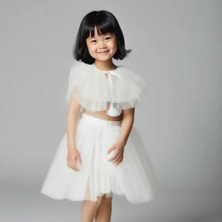 Young girl wearing a white dress with a sheer overlay against a gray background