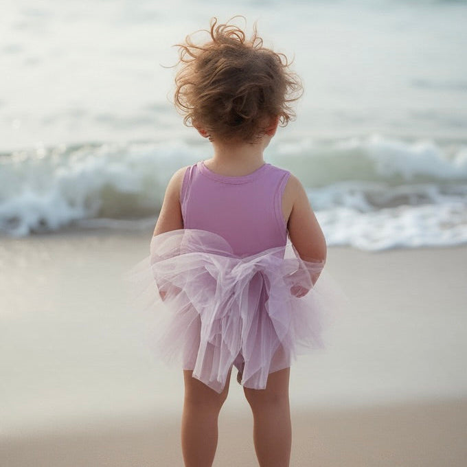 Child in a pink dress standing on a beach with waves in the background