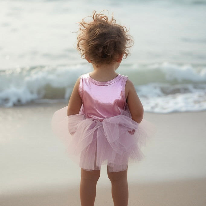 Child in a pink dress standing on a beach with waves in the background