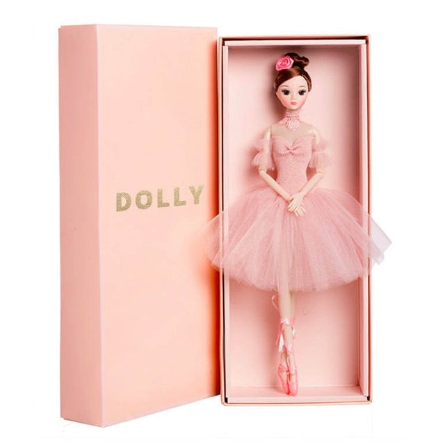 A doll named DOLLY wearing a pink tutu dress, placed inside a pink box with the DOLLY brand name on it.