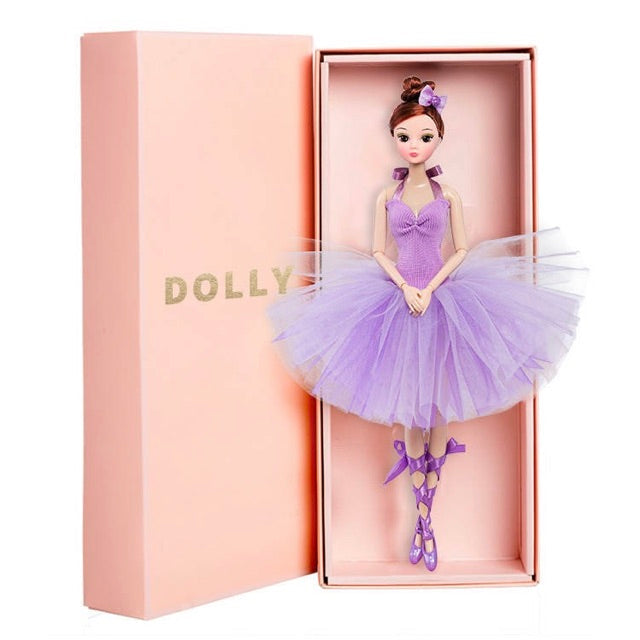 A doll named DOLLY® with a purple tutu dress, displayed inside its pink packaging box.