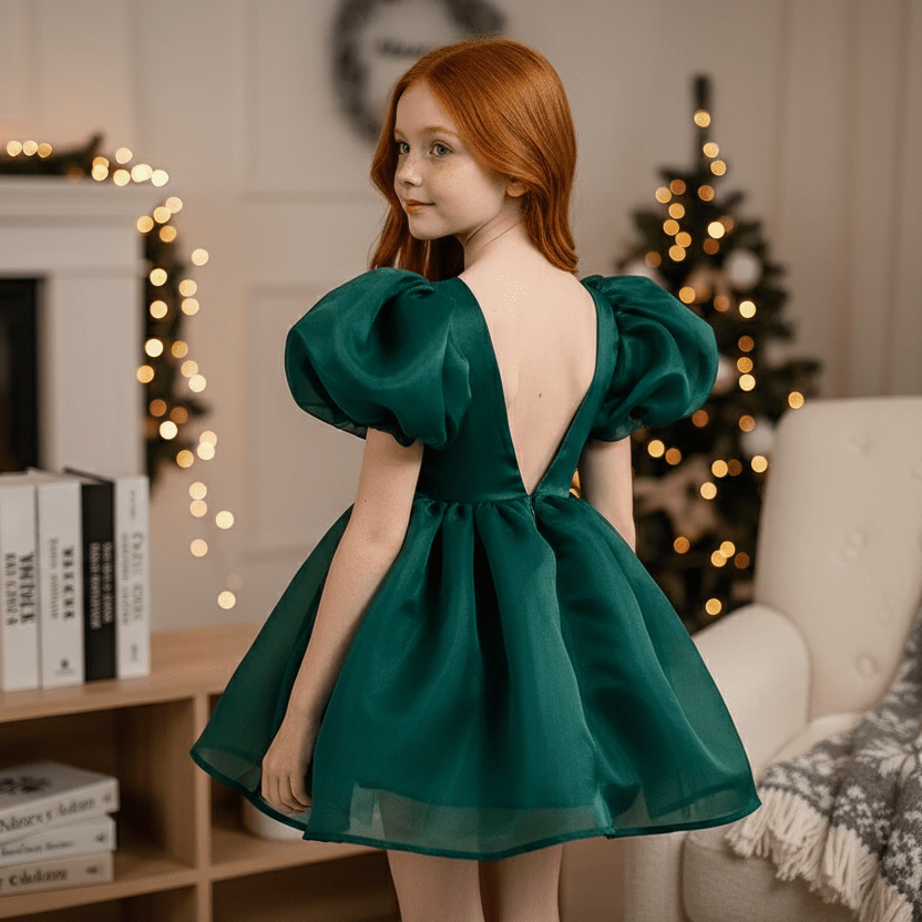 Young girl in a green dress with puffed sleeves standing in a cozy room with festive decorations.