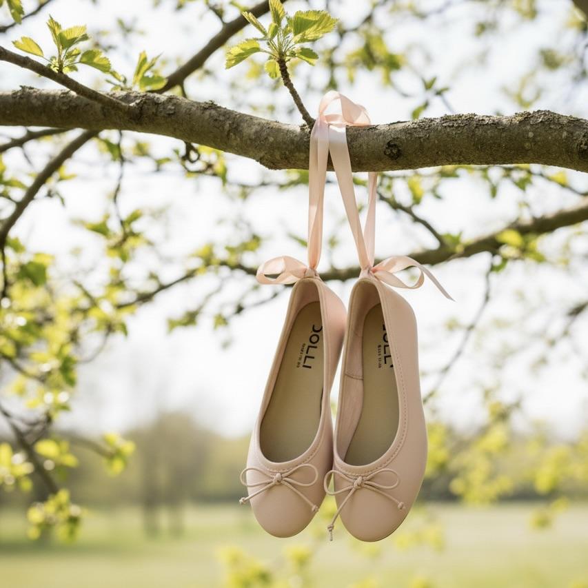 Pair of pink ballet flats with ribbons hanging from a tree branch in a park setting.