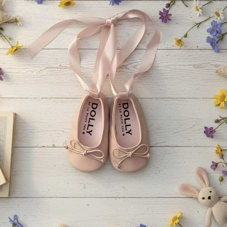 Pair of pink ballet shoes with ribbons on a wooden surface with flowers and a toy rabbit.