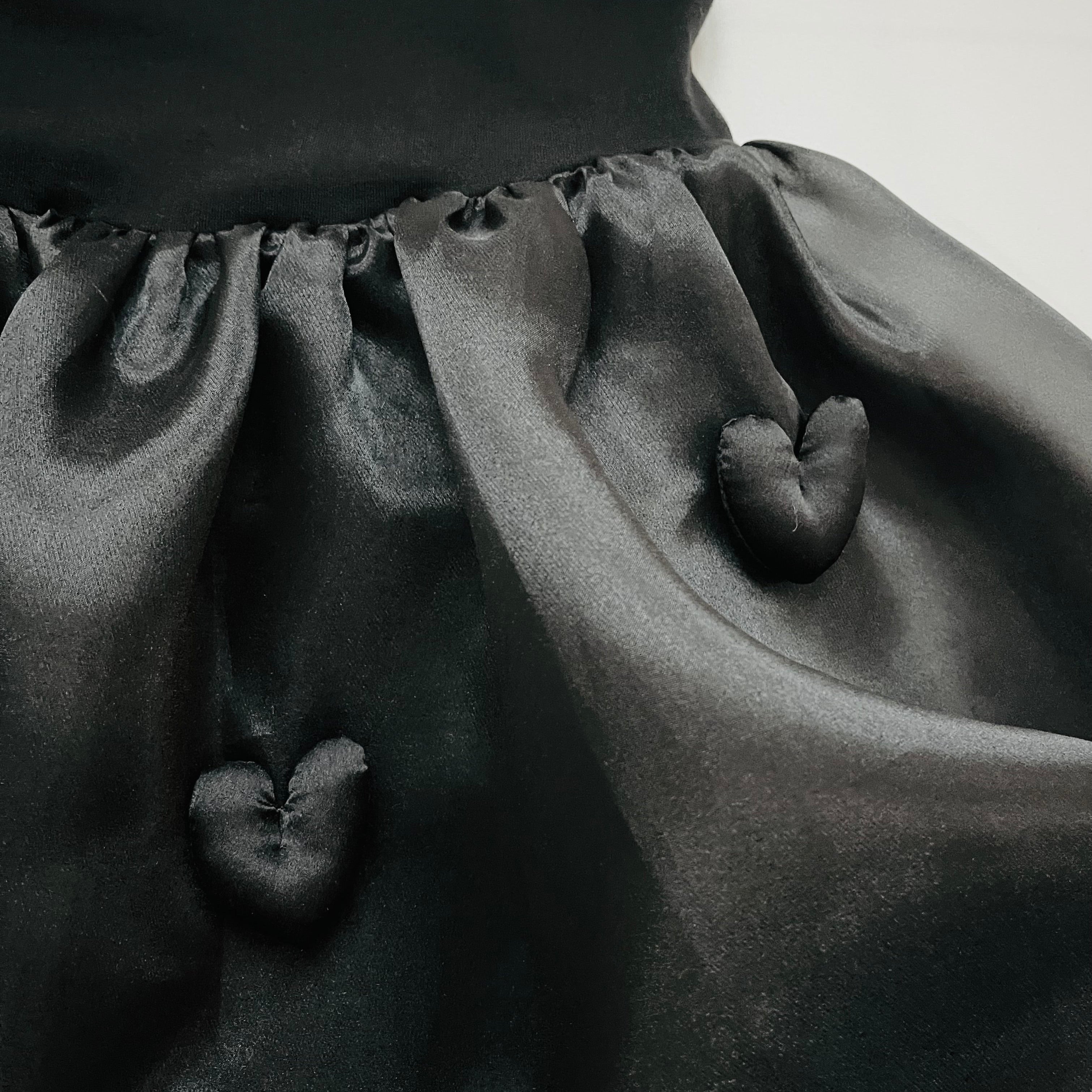 Close-up of a black dress with puffed sleeves and heart-shaped buttons on a white background