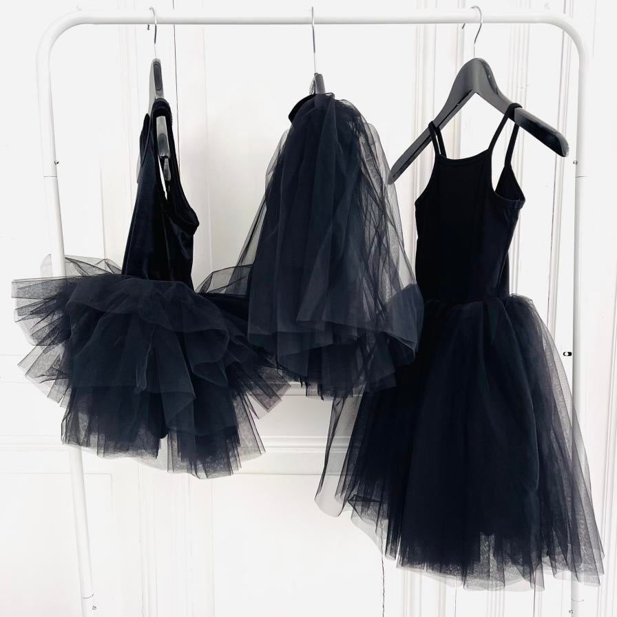 Black tutu dresses hanging on a rack against a white background
