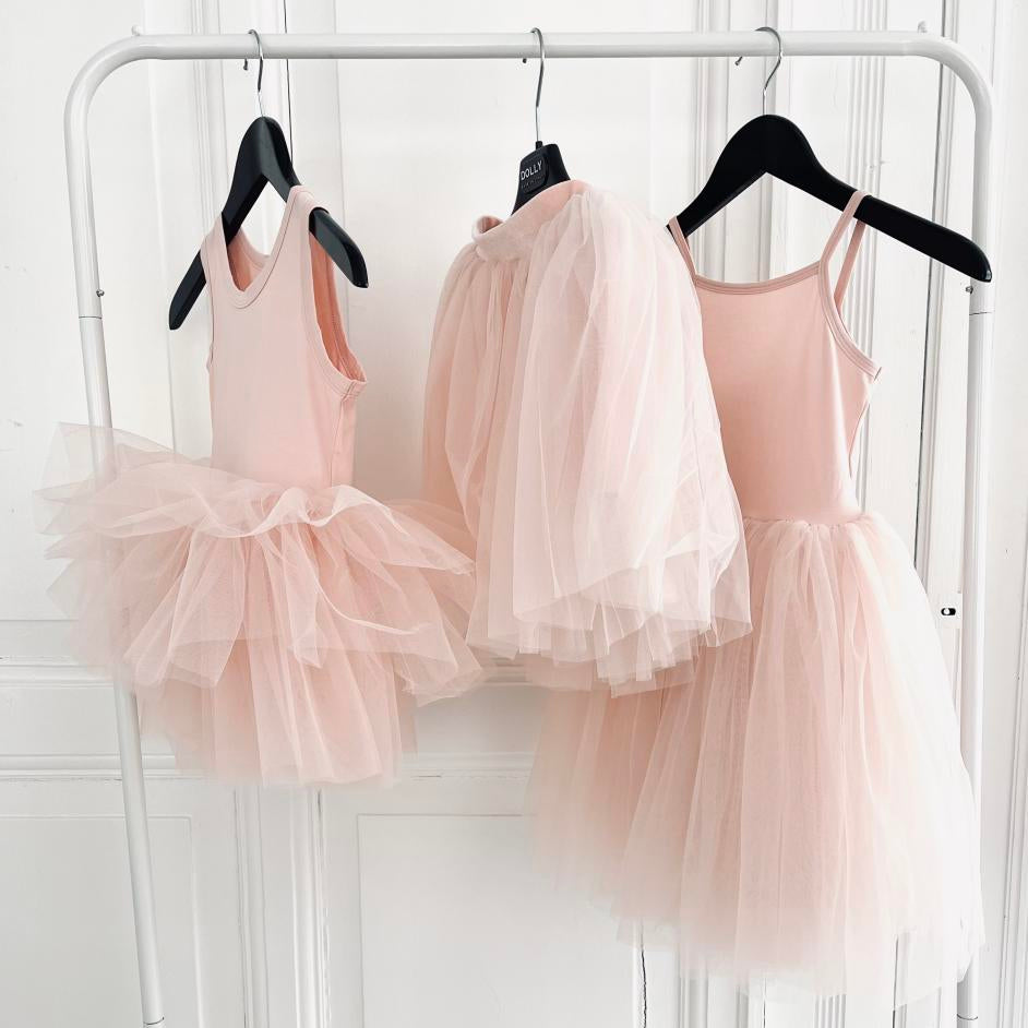 Three pink tutu dresses hanging on a rack against a white wall.