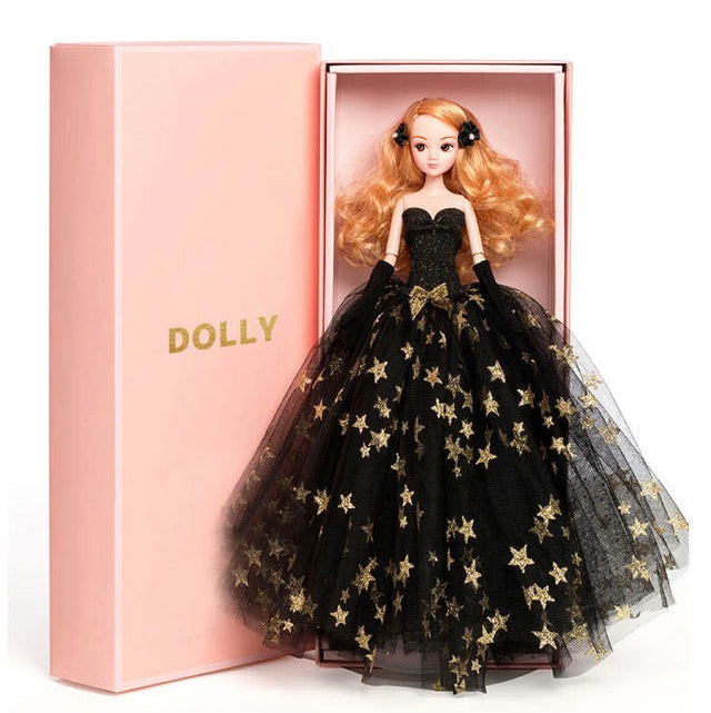 A fashion doll with golden blonde hair, dressed in a black tulle dress with gold stars, presented in a pink DOLLY® branded box.