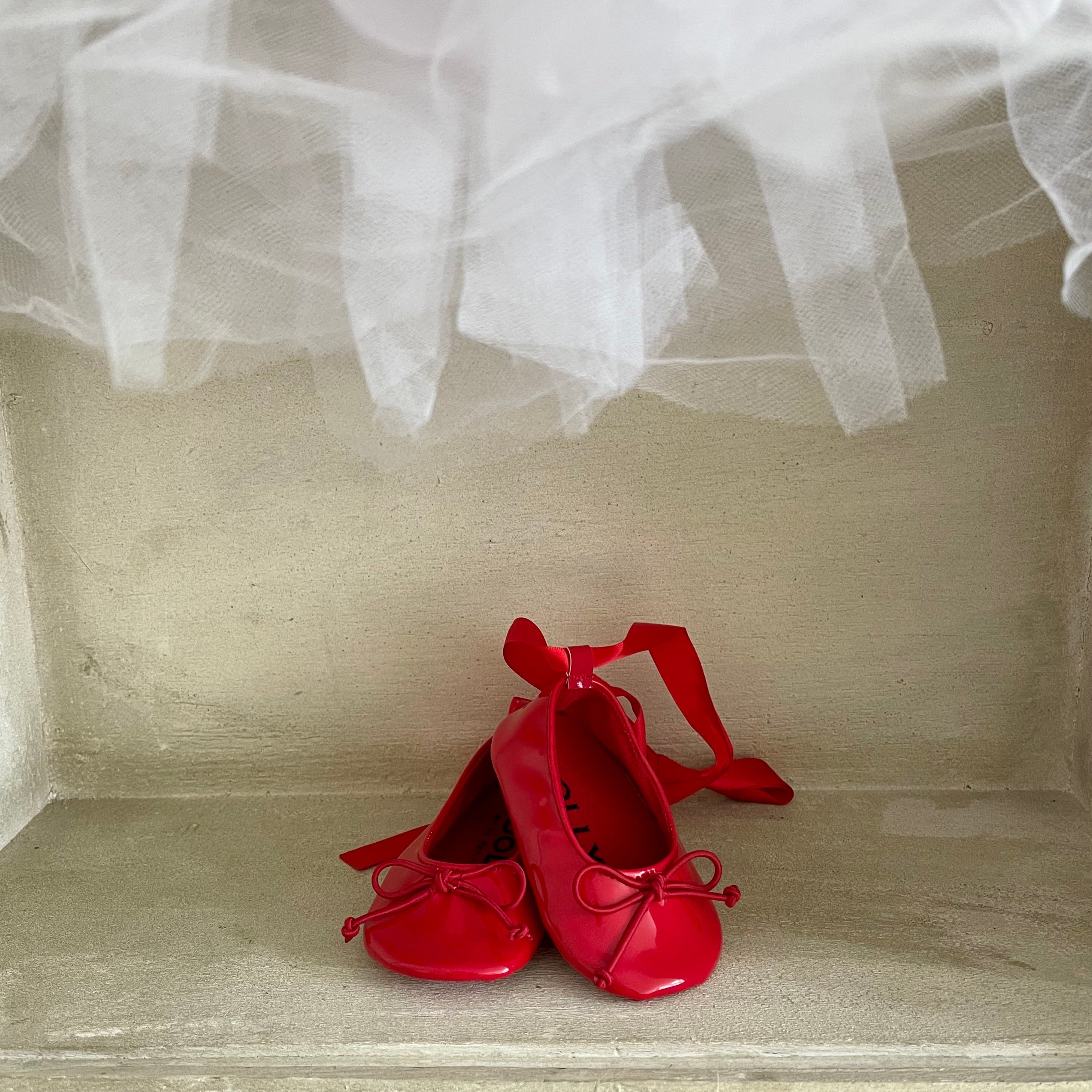 Red shoes with ribbons on a textured surface with white fabric draped over it