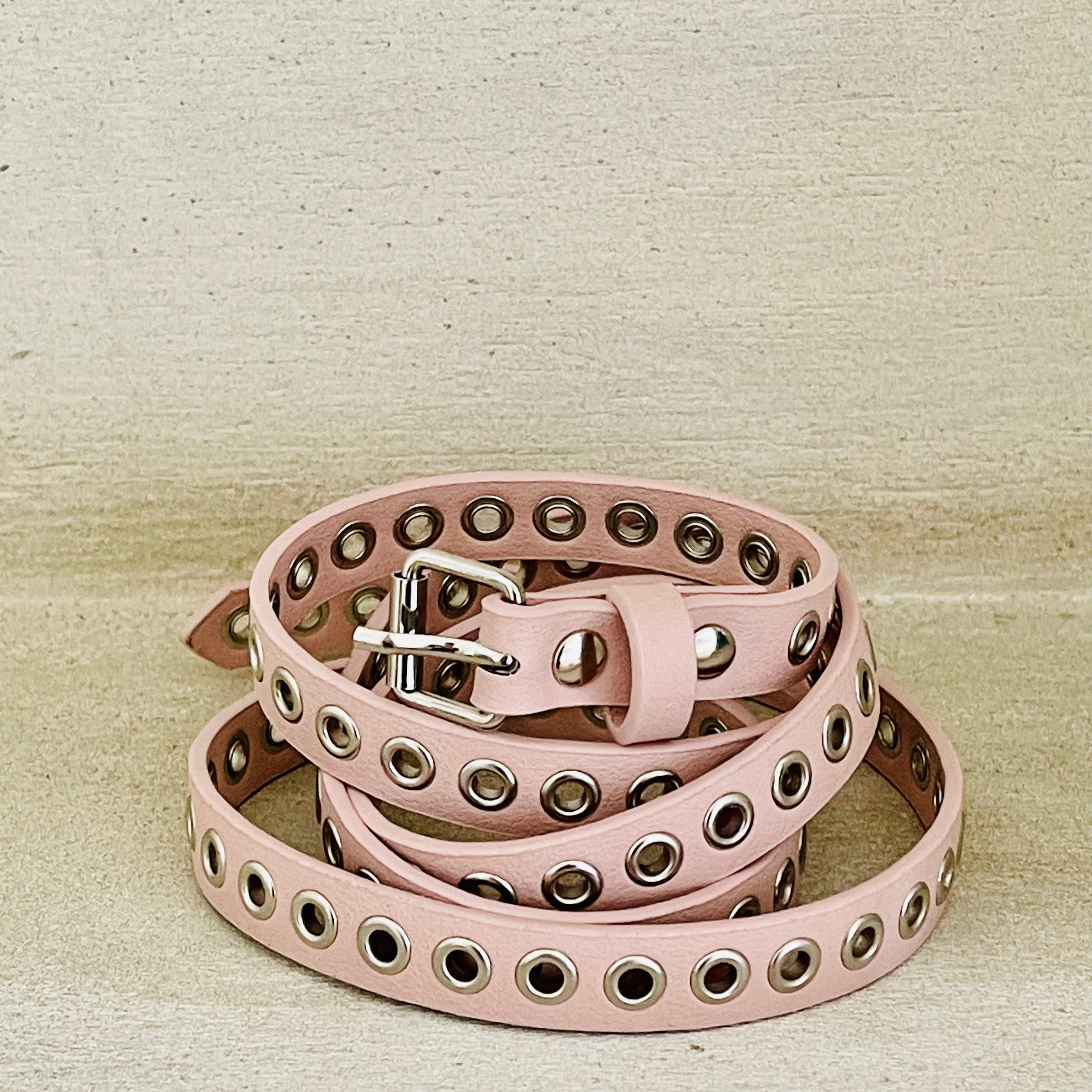 Pink leather belt with grommets on a beige background