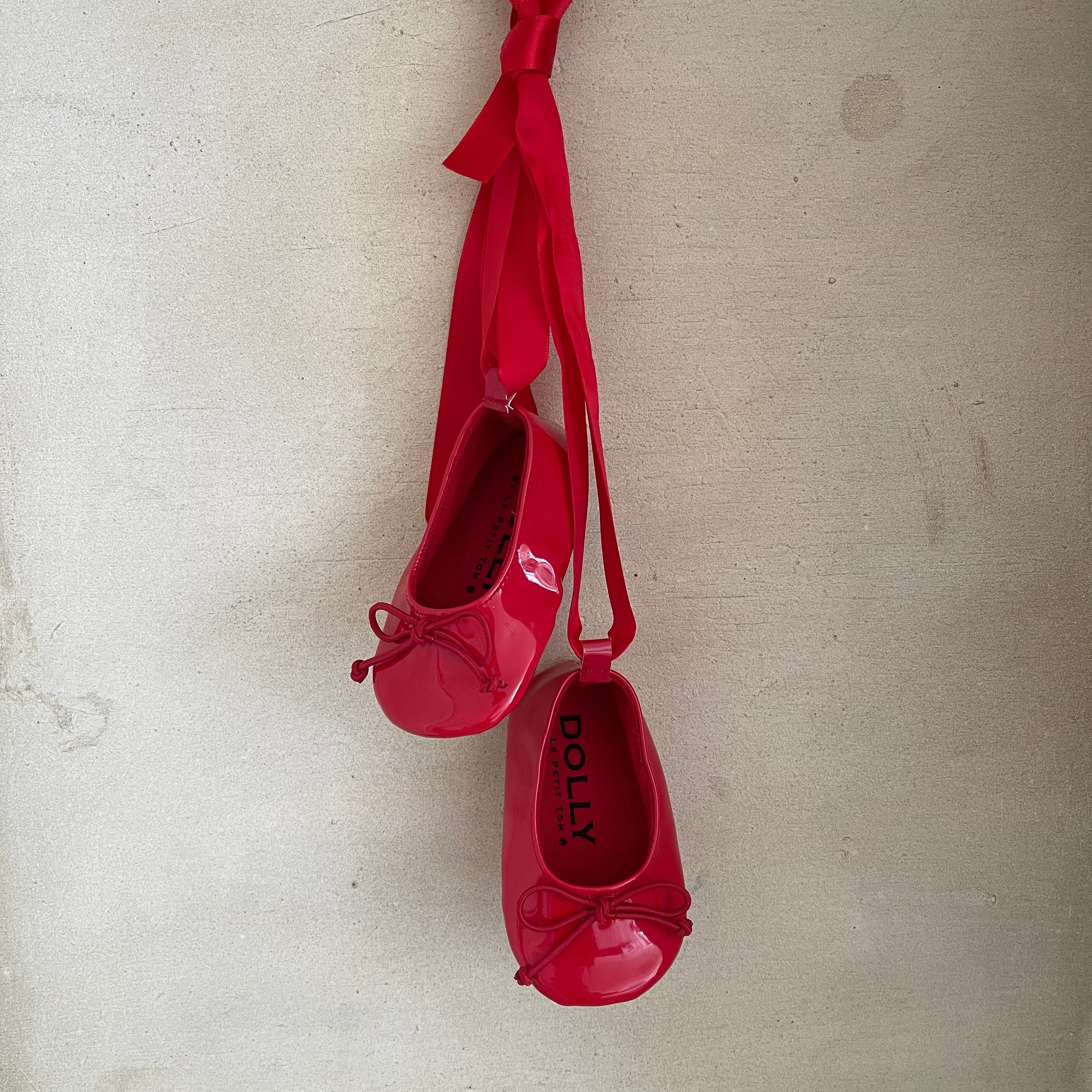 Red ballet shoes with ribbons hanging on a textured beige wall