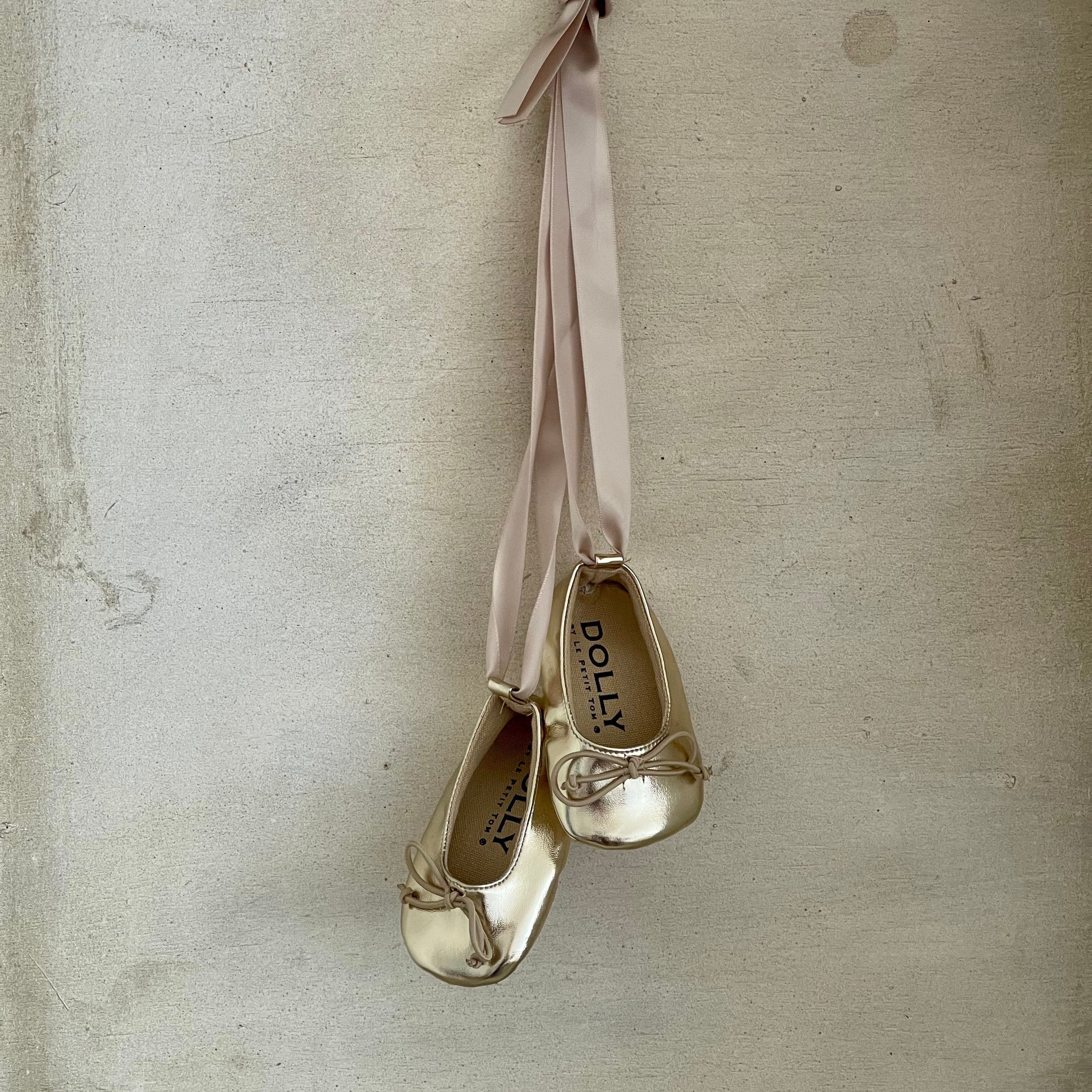 Gold shoes with ribbons hanging against a textured beige wall
