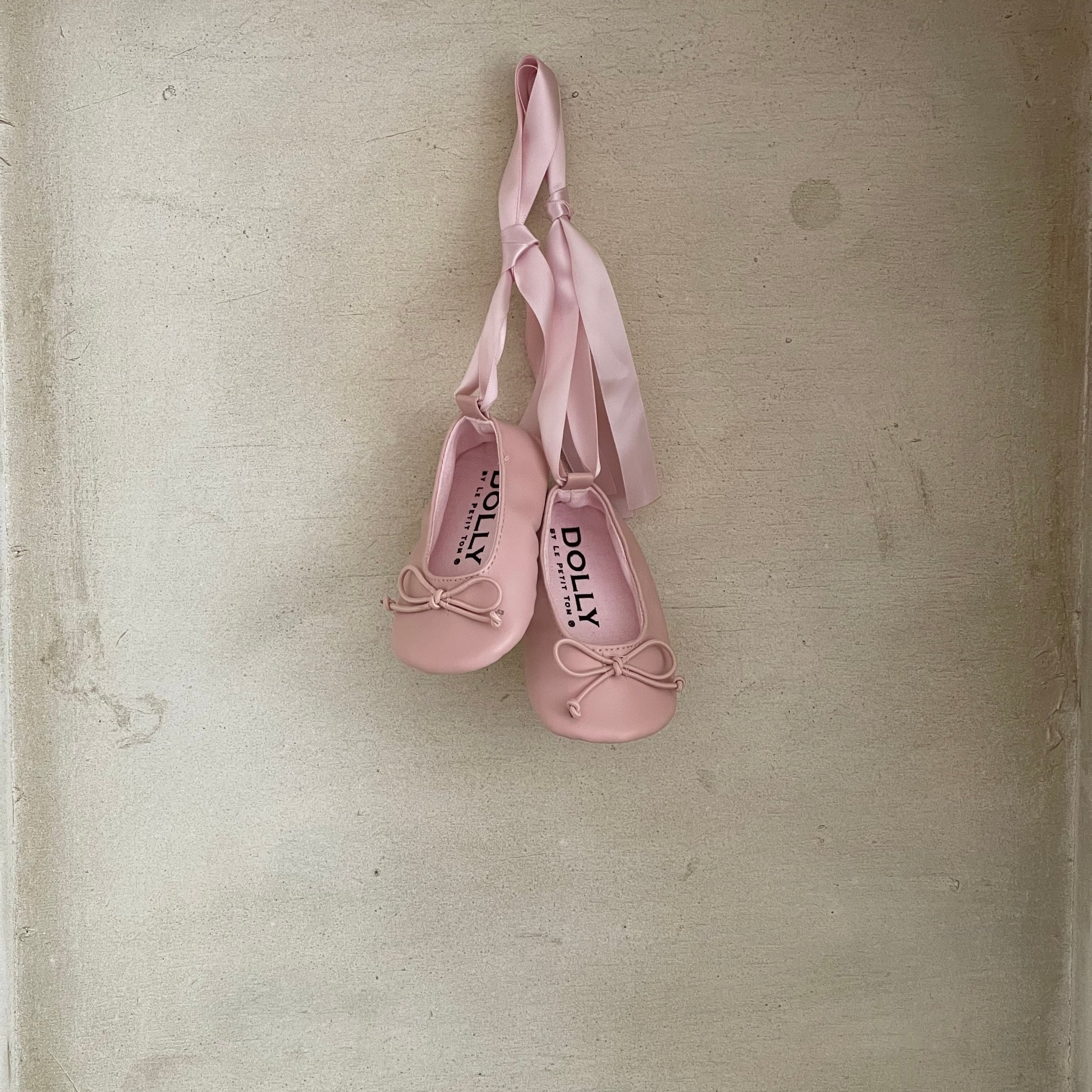 Pair of pink ballet shoes with ribbons on a beige surface