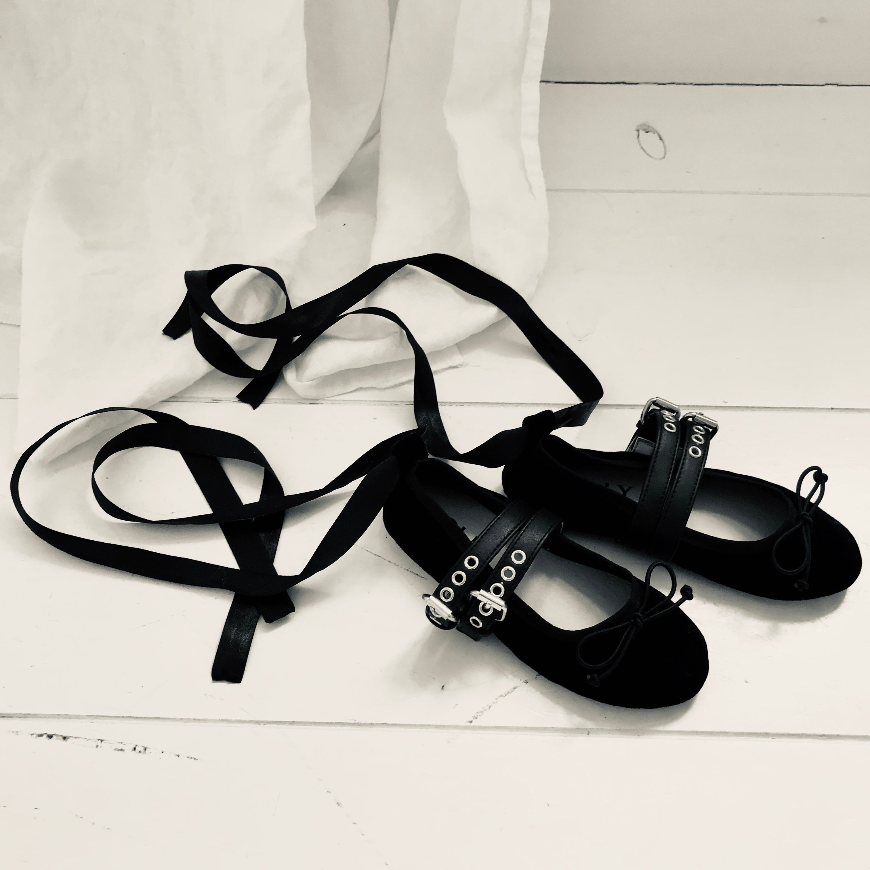 Black ballet shoes with ribbons on a white wooden floor