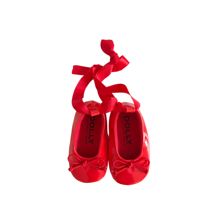 A pair of red baby ballerina shoes with ribbons tied at the front, on a white background with the text 'DOLLY Le Petit Tom ®' at the bottom.