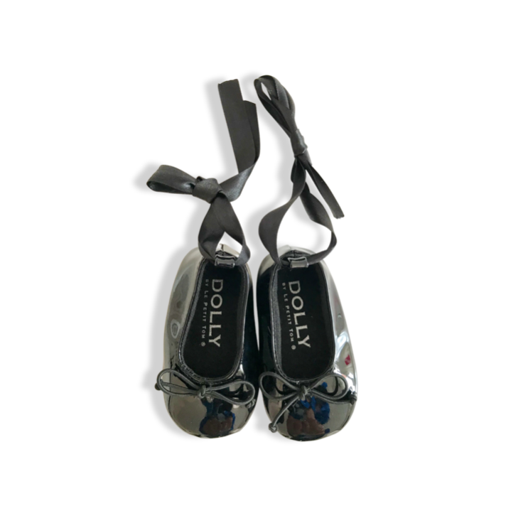 Pair of black ballet flats with ribbons on a white background, branded 'Dolly'.