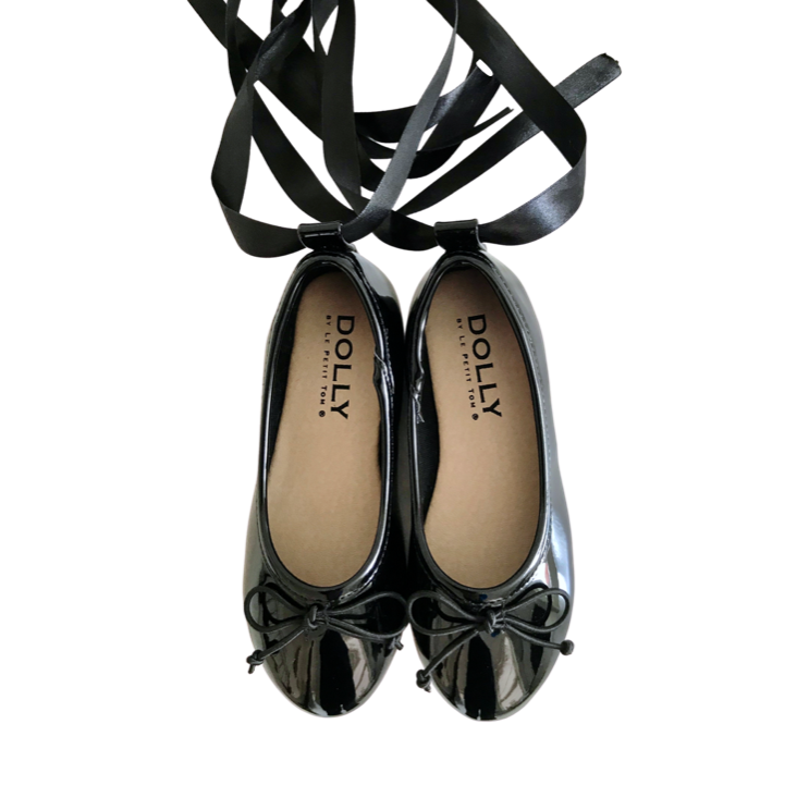 A pair of black DOLLY by Le Petit Tom ballerina flats with two satin ribbons and the brand's exclusive I'M DOLLY grosgrain ribbon tied in a bow.