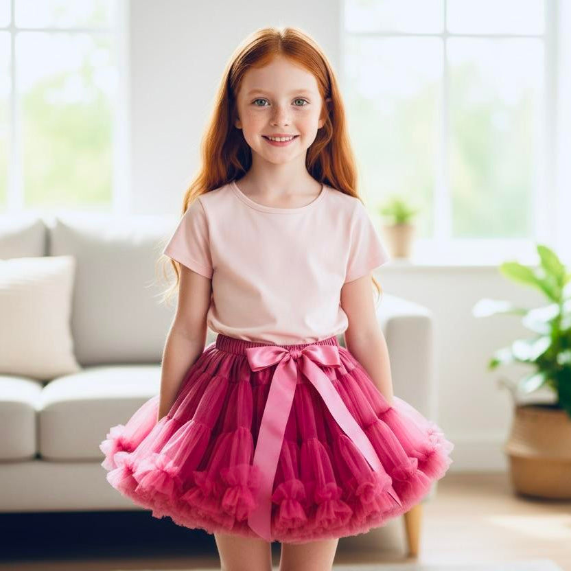 Young girl in a pink top and red tutu skirt standing in a bright living room.