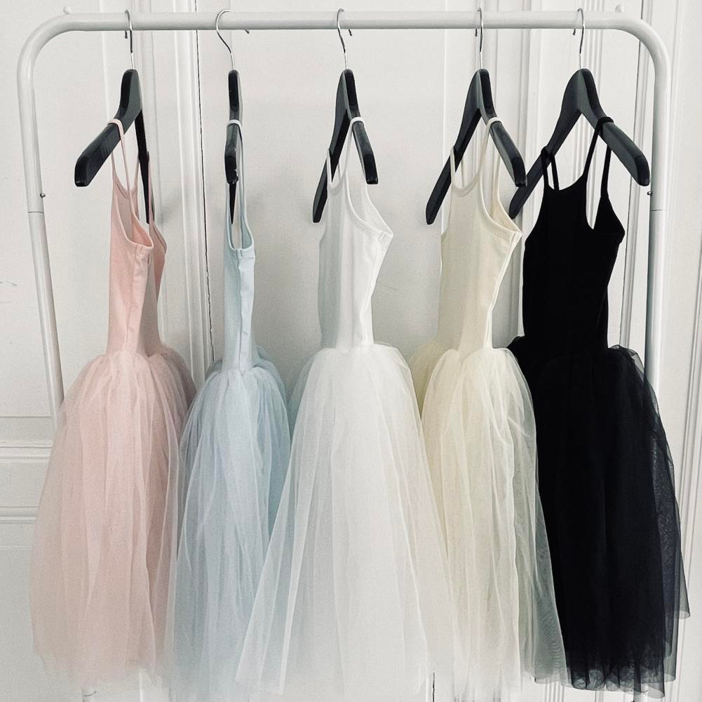 Five dresses in different colors hanging on a rack against a white wall.
